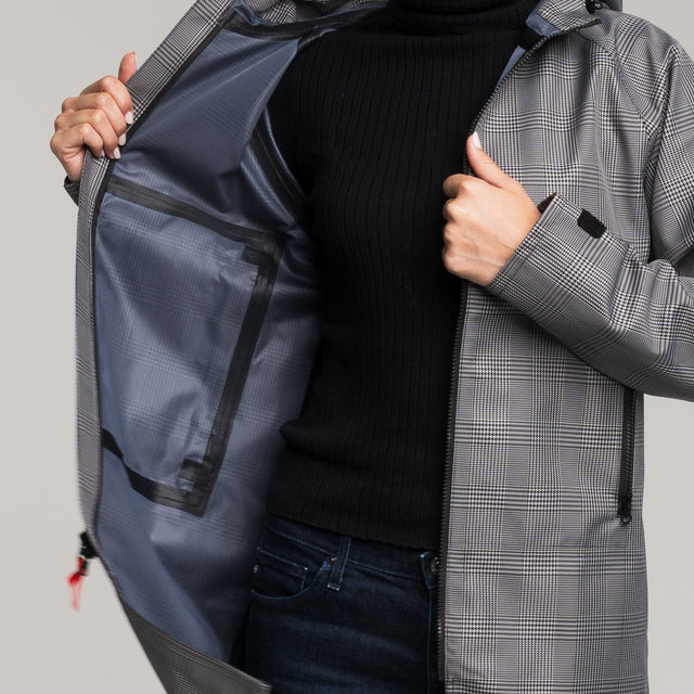 Person wearing a gray checkered coat with a black sweater and blue jeans, holding a navy duffel bag.