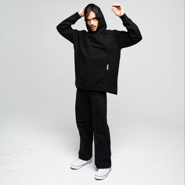 Person wearing a black hoodie and pants in a studio setting