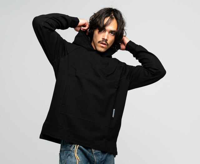 Man wearing a black hoodie and blue jeans standing against a white background