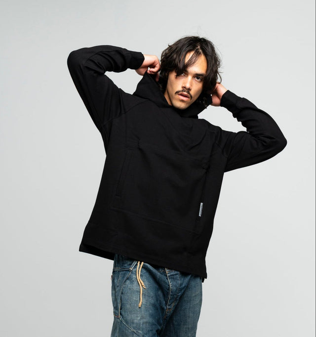 Person wearing a black hoodie and blue jeans standing against a white background