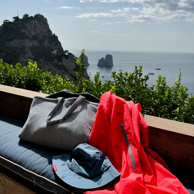 Electric Flamingo Zipster Jacket and I Am Blue Bucket Hat from Cleverhood draped in front of scenic view
