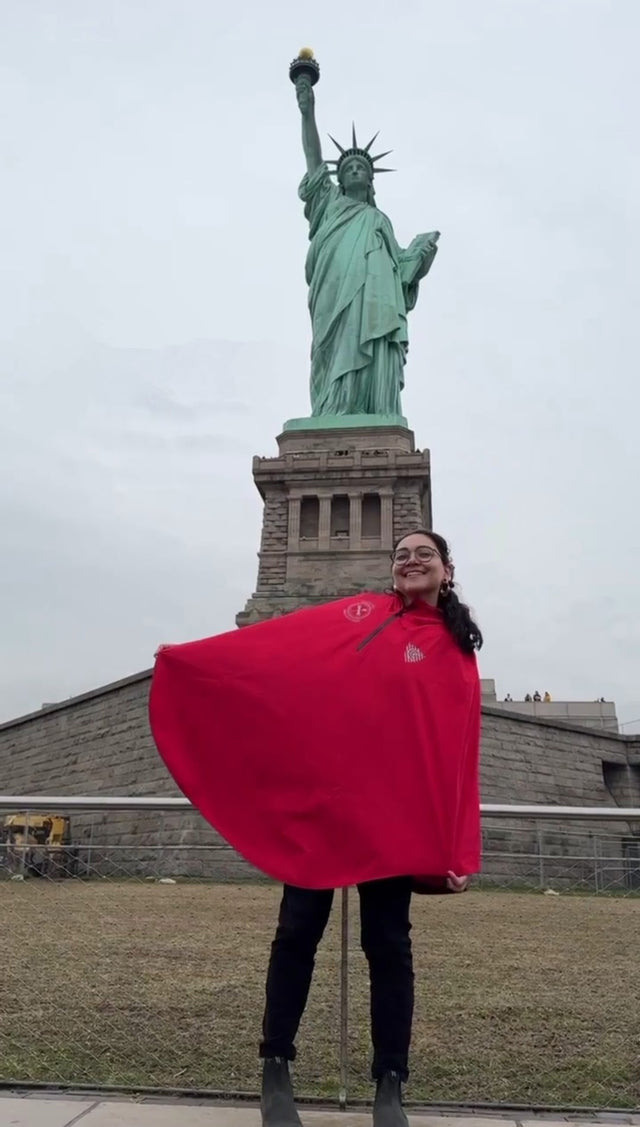 Woman wearing Randy Red Somerville Bike Kitchen Rover Rain Cape from Cleverhood in front of Statue of Liberty