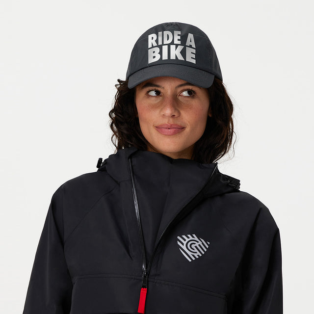 Person wearing a black jacket with a logo and a cap with 'RIDE A BIKE' text on a white background