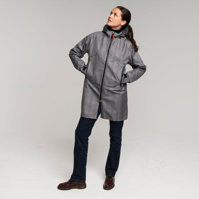 woman wearing a gray houndstooth trench coat standing against a white background