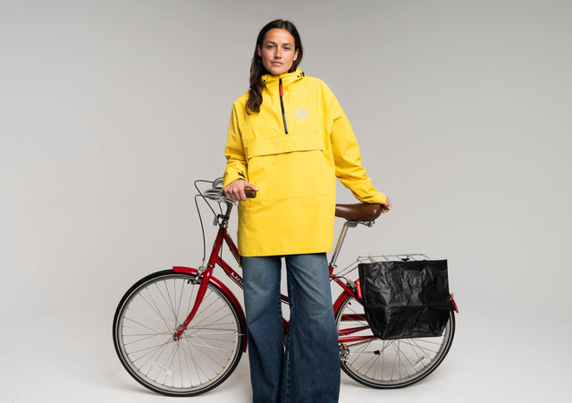 Woman wearing a yellow rain anorak next to a red bicycle with a pannier