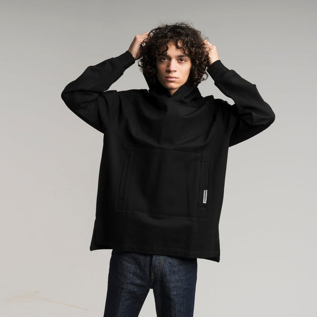 Person wearing a black oversized sweater and dark jeans on a white background