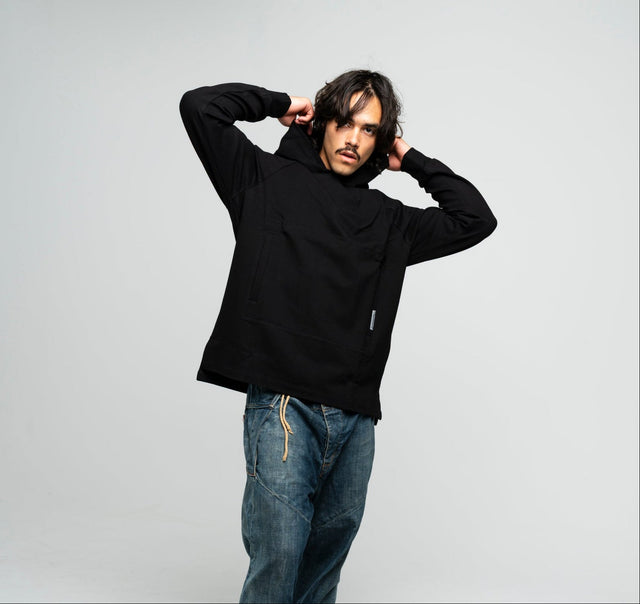 Person wearing a black hoodie and blue jeans against a plain background